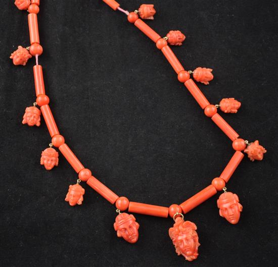 A late 19th/early 20th century coral baton and bead link necklace, hung with fourteen graduated double sided carved mask charms,